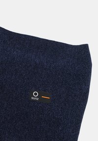 Tessuto lavorato a maglia blu scuro con una texture liscia. Presenta un'etichetta nera con un accento arancione che mostra "sun2". Design semplice e privo di decorazioni.
