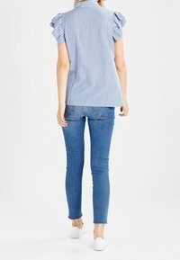 Modrá a bílá pruhovaná blůzka s volány na krátkých rukávech, doplněná o světle modré skinny džíny a bílé slip-on boty.