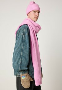 Rožinė megzta kepurė ir šalikas derinami su džinsine striuke. Rudi vilnoniai pirštinės su etikete. Paprasta, jauki lauko apranga.