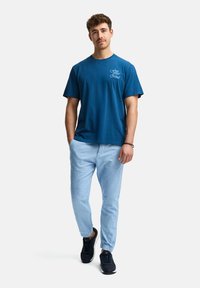 Camiseta de algodón azul con el texto "Libera tu mente", combinada con pantalones de lino azul claro y zapatillas negras, con un corte relajado y un diseño sencillo.