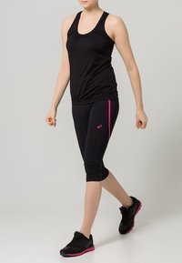 Black athletic tank top with gathered detail, paired with black capri leggings featuring pink side stripes. Worn with black athletic shoes.