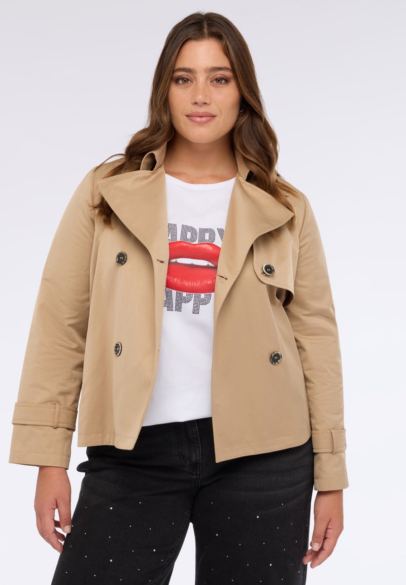 Ljusbeige trenchcoat med spetsig krage och dubbelknäppt design. Har svarta knappar och en mjuk, slät tygtextur.