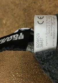 Brown suede material with a textured surface, featuring a black tag with white lettering and a care label with printed details.