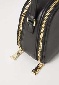 Borsa in pelle nera texture con doppia cerniera dorata, dettagli in metallo e un design rettangolare elegante. Le linguette delle cerniere sono di forma triangolare.