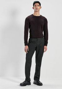 Dark brown, long-sleeve sweater paired with black trousers and black lace-up shoes. The sweater has a round neckline and fitted design.