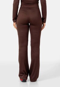 Bruine geribbelde flared broek met een hoge taille, gemaakt van rekbare stof en subtiele verticale textuur, gecombineerd met donkere sneakers.
