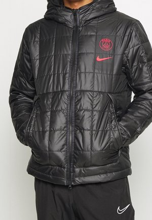 Schwarze gesteppte Jacke mit Kapuze, durchgehendem Reißverschluss, rotem Paris Saint-Germain-Logo und Nike-Swoosh, kombiniert mit schwarzen Nike-Hosen.