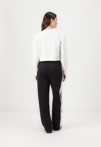 Valge lühike sweatshirt ja mustad püksid kreemika külgmise triibuga. Pükstel on lõdvalt istuv siil ja tagakotid.