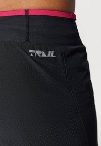Schwarze Active-Shorts mit einem rosa elastischen Bund, ausgestattet mit perforierter Textur und einem reflektierenden "TRVL"-Logo an der Seite.
