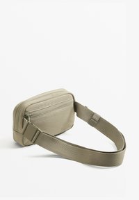 Borsa a tracolla in tessuto beige con una superficie liscia, dotata di un compartimento con zip e una tracolla regolabile. Design compatto e rettangolare.