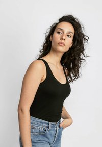 Top nero senza maniche con scollatura rotonda, realizzato in tessuto elasticizzato. Un paio di jeans blu a vita alta, caratterizzati da una vestibilità comoda e un lavaggio chiaro.