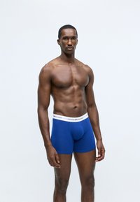 Blå bomull boxershorts med en vit midjeband som har logotext. Designen är figurnära med en slät textur.