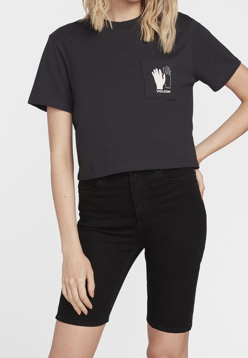 Czarny skrócony T-shirt z przednią kieszenią, ozdobiony białymi grafikami dłoni oraz napisem "VOLCOM". Połączony z czarnymi szortami z wysokim stanem.