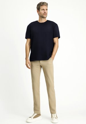 Camiseta azul marino de manga corta, de corte relajado; pantalones beige de tejido suave, combinados con zapatillas blancas con detalles en marrón.