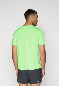 Αθλητικό μπλουζάκι με κοντό μανίκι σε λαμπερό πράσινο χρώμα, κατασκευασμένο από ελαφρύ ύφασμα. Διαθέτει στρογγυλή λαιμόκοψη και πλαϊνές σχισμές για ευελιξία.