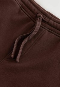 Pantalons de survêtement en coton marron avec un cordon de serrage à bout noué, texture lisse et taille élastique.