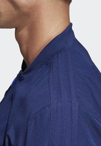 Dunkelblaues Sportjackett mit hohem Kragen, strukturiertem Stoff und vertikalen Streifen auf den Schultern, entworfen für eine figurbetonte Passform.