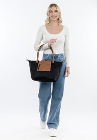 Borsa tote nera in nylon con dettagli in pelle marrone. Caratterizzata da una tasca frontale e manici doppi, su uno sfondo chiaro.