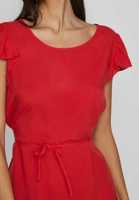 Vestido rojo hecho de una tela ligera con un escote redondo, mangas con volantes y un detalle de cintura atada. Textura suave y color vibrante.