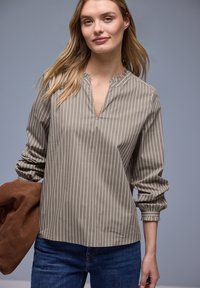 Blouse à manches longues beige et blanche à rayures, avec col en encoche, poignets froncés et coupe décontractée, associée à un jean denim bleu.
