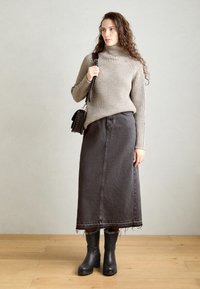 Bež pulover s rebrastim vzorcem, črna denim maksi krilo s strganim robom in črne gležnjarje. Model drži majhno črno torbico čez ramo.