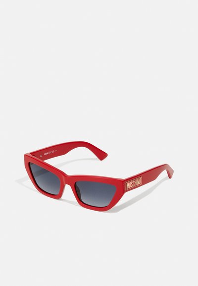 Ochelari de soare roșii cu finisaj mat, design unghiular în formă de ochi de pisică, lentile gri cu degradé și logo-ul auriu "Moschino" pe braț.