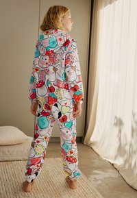 Tuta con cappuccio in morbido pile, con fantasie colorate di cartoni animati di cibo, animali e cuori su sfondo bianco. Vestibilità comoda con polsini.