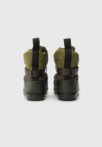 Botas de tornozelo verde-escuras com um colarinho acolchoado em estilo bungee, sola de borracha e detalhe de faixa elástica na parte de trás. Destaques em material texturizado.