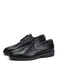 Un paio di scarpe eleganti da uomo in pelle nera lucida, con chiusura a lacci e suole basse impilate, su uno sfondo bianco.