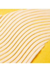 Fines bandes courbes de matériau beige clair superposées sur un fond jaune vif, mettant en valeur une texture lisse et un motif organisé.