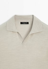 Polo en maille beige clair avec col ouvert et étiquette noire Massimo Dutti cousue au niveau du col.