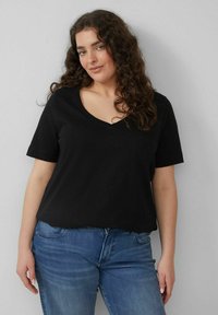 Schwarzes V-Neck-T-Shirt aus weichigem Baumwollmaterial, mit kurzen Ärmeln und lässiger Passform, kombiniert mit blauen Jeans.