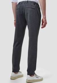 Mørkegrå sweatpants med tapered fit, elastisk talje og en baglomme. Sammen med hvide sneakers.