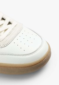 Baskets en cuir blanc avec une semelle en gomme texturée, dotées de petites perforations, de lacets plats et d'un design de capuchon de pied lisse.