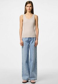 Beżowy prążkowany top na ramiączkach z szerokimi paskami, zestawiony z jasnoniebieskimi spodniami o wysokim stanie i szerokimi nogawkami oraz różowymi zamszowymi butami typu slip-on.