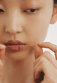 Collar de cadena de plata sostenido cerca de los labios, con pequeñas piedras preciosas rojas y un cierre delicado. El tono de piel es cálido, con una textura suave.