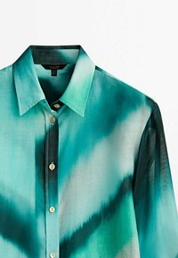 Chemise à manches longues boutonnée avec col classique, présentant un dégradé de motifs bleu sarcelle et vert foncé sur un tissu léger.