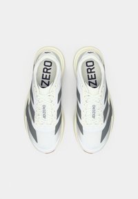 Λευκά αθλητικά παπούτσια με γκρι ρίγες, πλέγμα στην επάνω επιφάνεια, στρογγυλεμένη μύτη και επίπεδη λαστιχένια σόλα. Διαθέτουν κορδόνια και τη σήμανση «ADIZERO» στην εσωτερική σόλα.