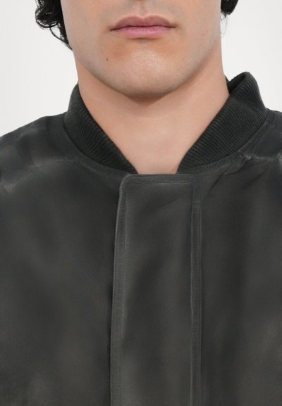 Must must jacket sujuva tekstuuriga, ribidega krae ja eesklapi kinnitusega; minimalistik disain ilma täiendavate mustriteta.