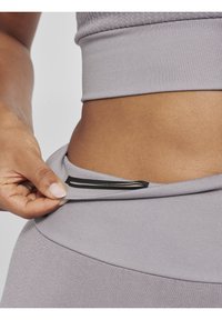 Grå atletisk crop top med en glat tekstur, der har en indvendig lomme sikret med et sort elastisk bånd, hvilket fremhæver dens funktionelle design.