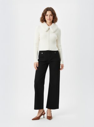Maglione bianco a coste con colletto in pelliccia sintetica, abbinato a pantaloni neri a vita alta e gamba larga e scarpe con tacco marroni.