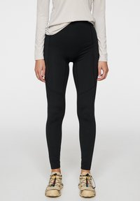 Svarta leggings med hög midja, slät yta och sömdetaljer, kombinerat med beigea sportskor med färgglada accenter.