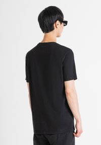 Camisa de algodón de manga corta en negro, con cuello redondo y el nombre de la marca "Morato" impreso de manera sutil en la parte posterior del escote.