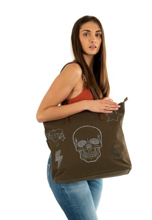 Bolsa de tote en verde oliva con diseños de calaveras y flores, con acentos de rhinestones plateados y asas de cuero marrón.