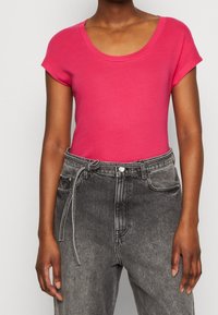 Lyserød kortærmet t-shirt med rund halsudskæring, parret med høj talje sorte denimjeans med bindebånd og en falmet tekstur.