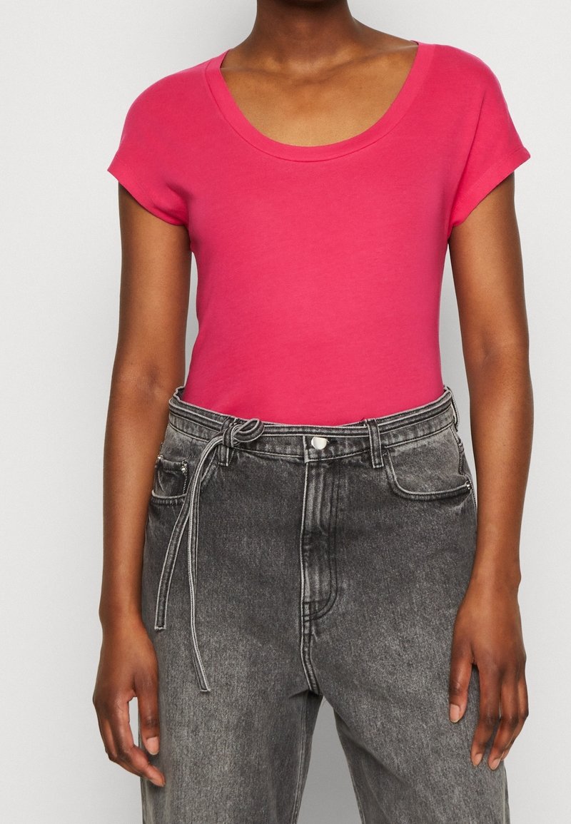 Lyserød kortærmet t-shirt med rund halsudskæring, parret med høj talje sorte denimjeans med bindebånd og en falmet tekstur.