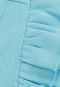 Vaalean sininen neulottu kangas, jossa on röyhelökoriste yhdellä reunalla ja ribbikuvio. Läheltä otettu yksityiskohta korostaa pehmeyttä ja muotoilua.