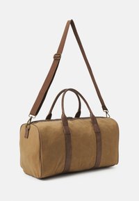Sac de voyage en toile marron avec des accents en cuir marron, poignées doubles, bandoulière ajustable et fermeture éclair. Texture lisse. Forme rectangulaire.