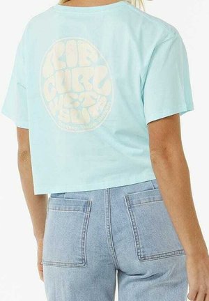 Osoba ubrana w jasno niebieski krótki T-shirt z wyblakłym okrągłym nadrukiem z tekstem oraz jasnoniebieskie, wysokie dżinsy z dużymi tylnymi kieszeniami.