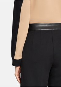 Dwukolorowa bluzka z czarnym rękawem i beżowym korpusem, z gładkim czarnym paskiem z sztucznej skóry i dopasowanymi czarnymi spodniami.